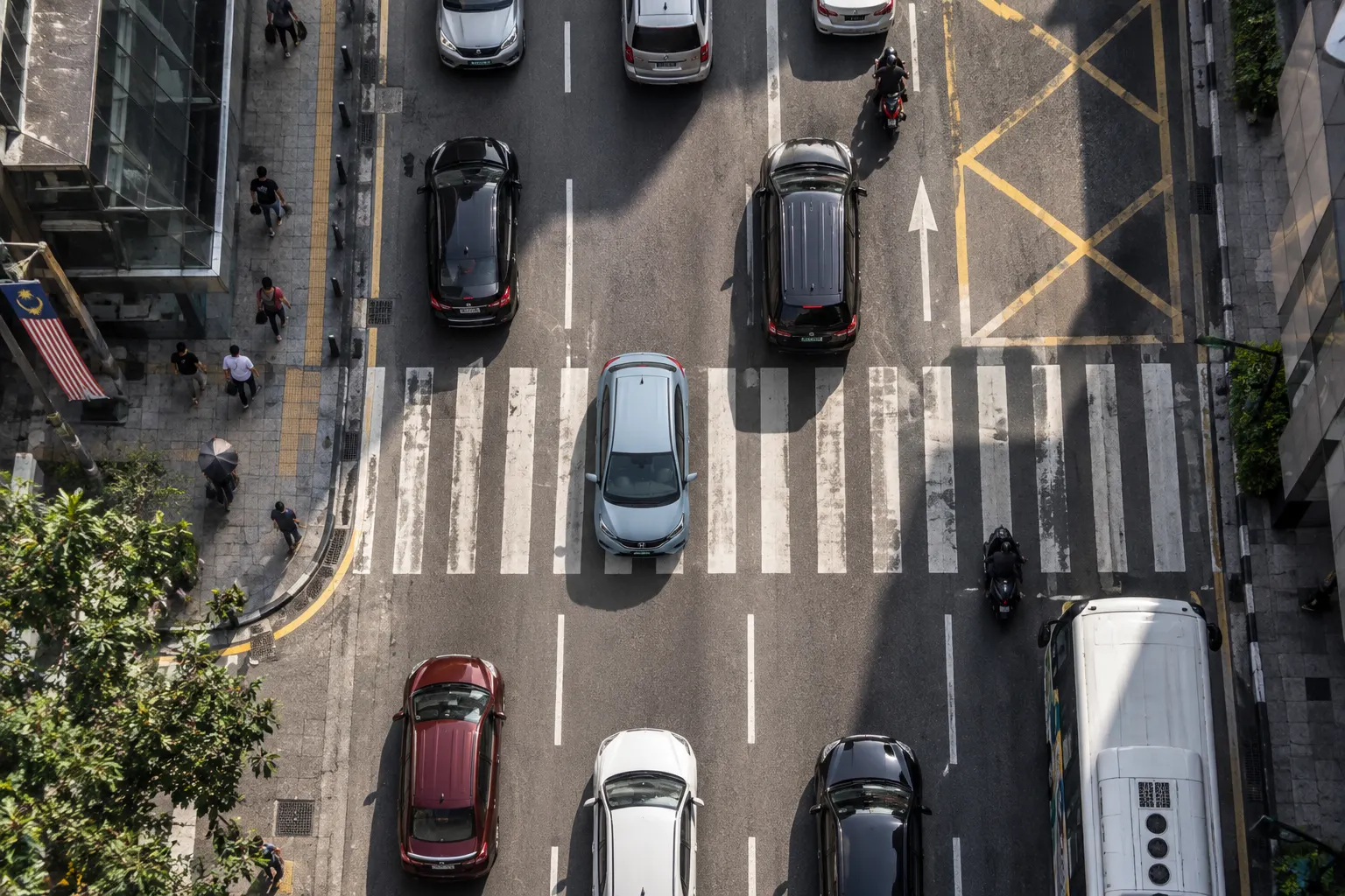 Top-down drone view of cars crossing a zebra crossing on a busy Kuala Lumpur street — car rental kuala lumpur