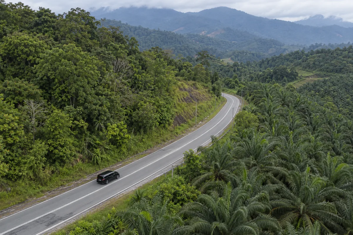 Aerial view of a black electric MPV, a Zeekr 009, driving on a winding road through palm-oil plantations and jungle hills near Genting Highlands for an electric car vs petrol car rental Malaysia comparison