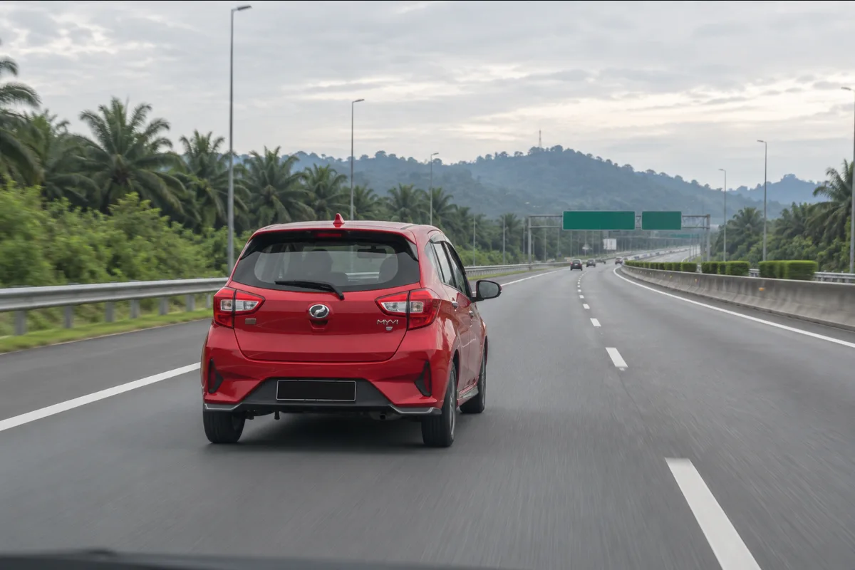 Red Perodua Myvi seen from behind driving on a Malaysian expressway in the early morning after an airport hand-over