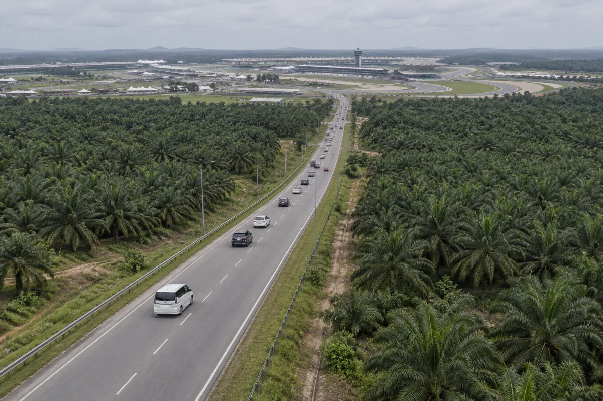 MotoGP Malaysia 2026 car rental drive: a white Nissan Serena S-Hybrid on the road through palm plantations towards Sepang International Circuit, seen from above